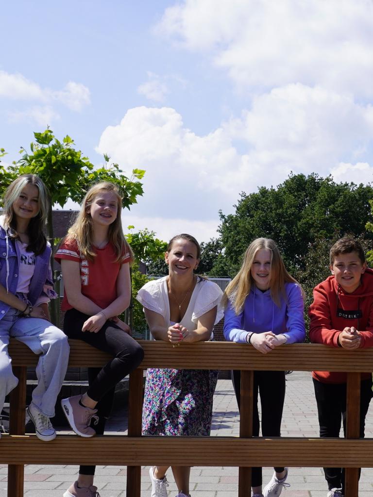 Leerlingen en docent op schoolplein achter hekje bomen op de achtergrond